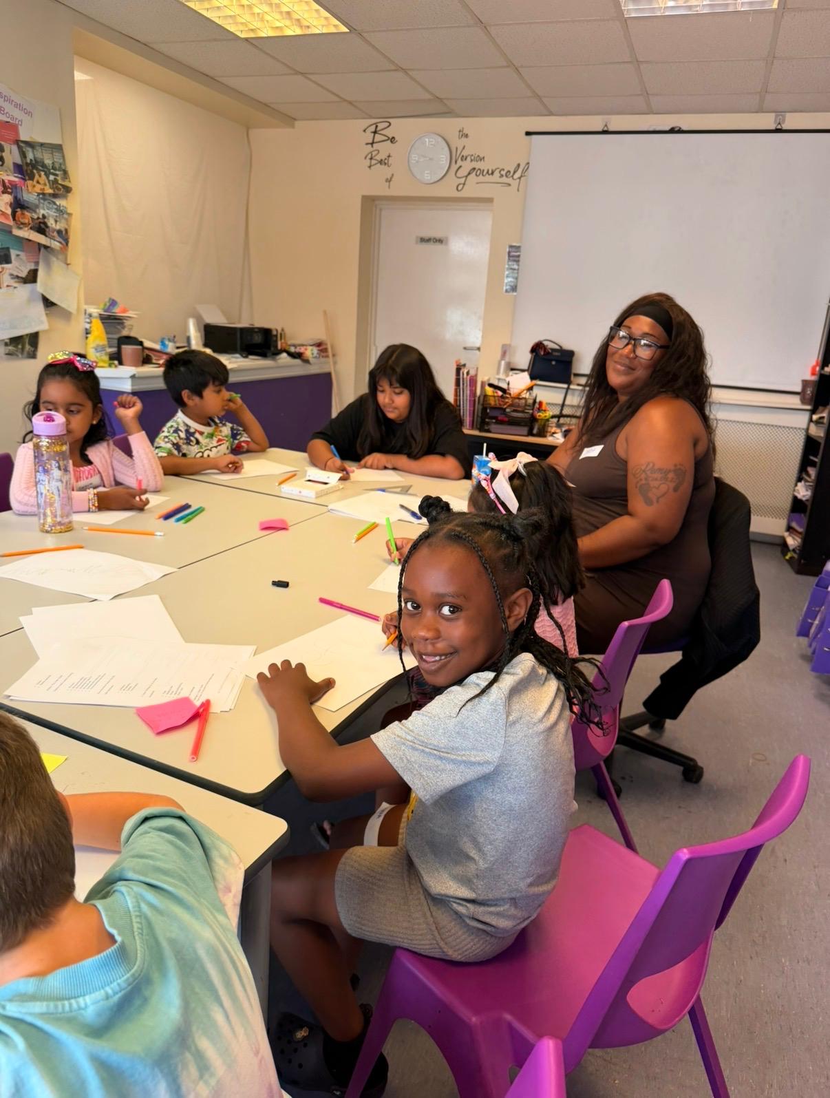 Children seated around a table with paper and colouring pens working on their own designs, with a facilitator nearby
