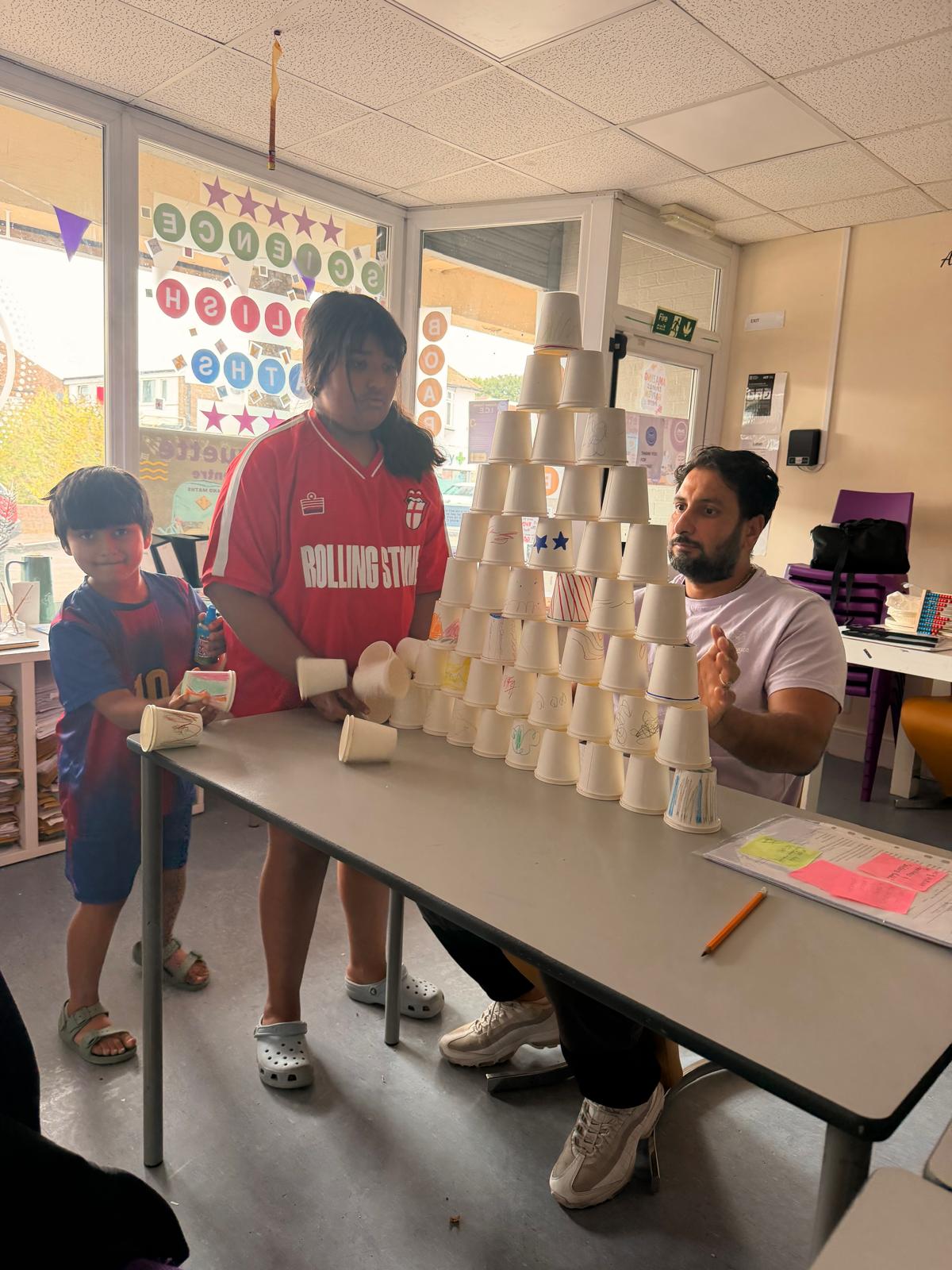 A volunteer and children building a cup pyramid challenge