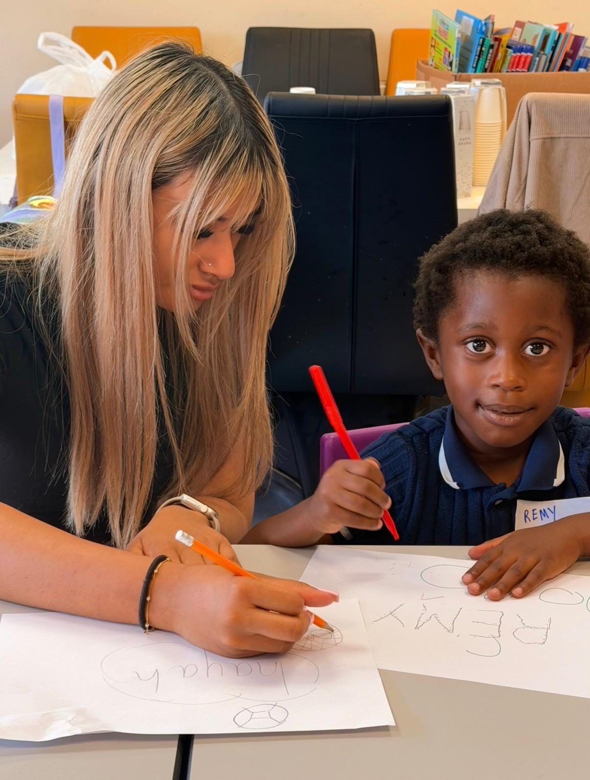 An adult drawing a shield design on paper alongside a young child holding a red pen